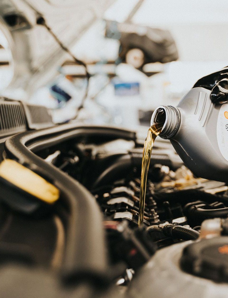 Close-up of a mechanic pouring engine oil into a car engine in an auto repair shop.