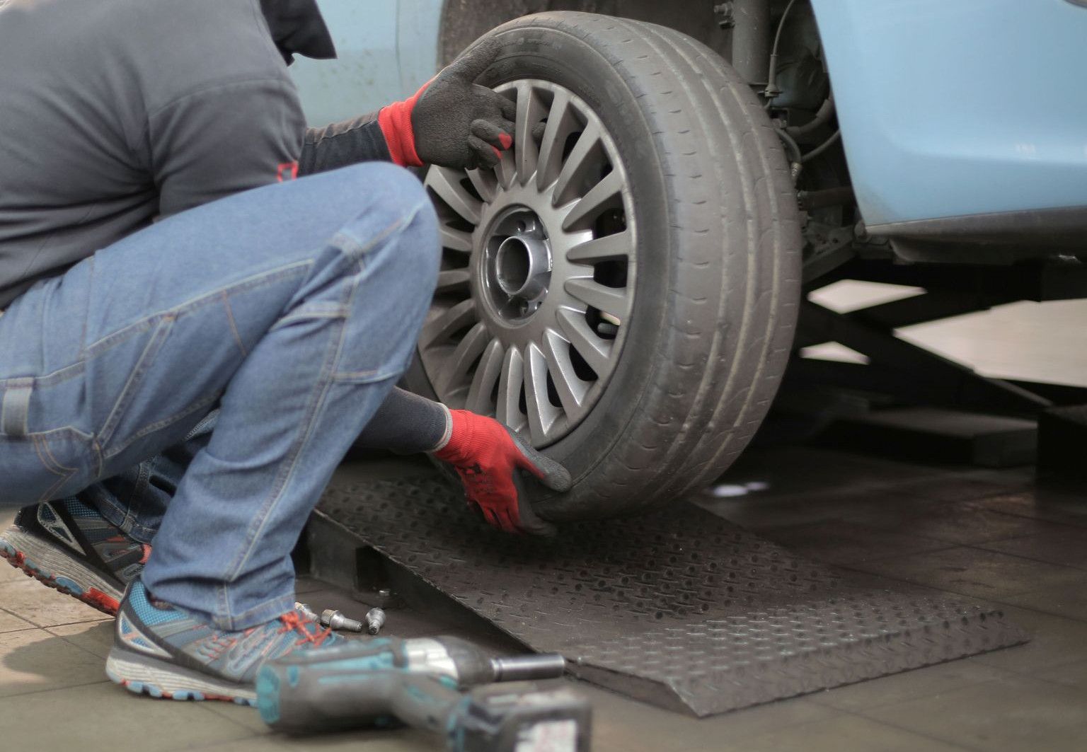 Mechanic changing a car tire indoors, using tools for vehicle maintenance.