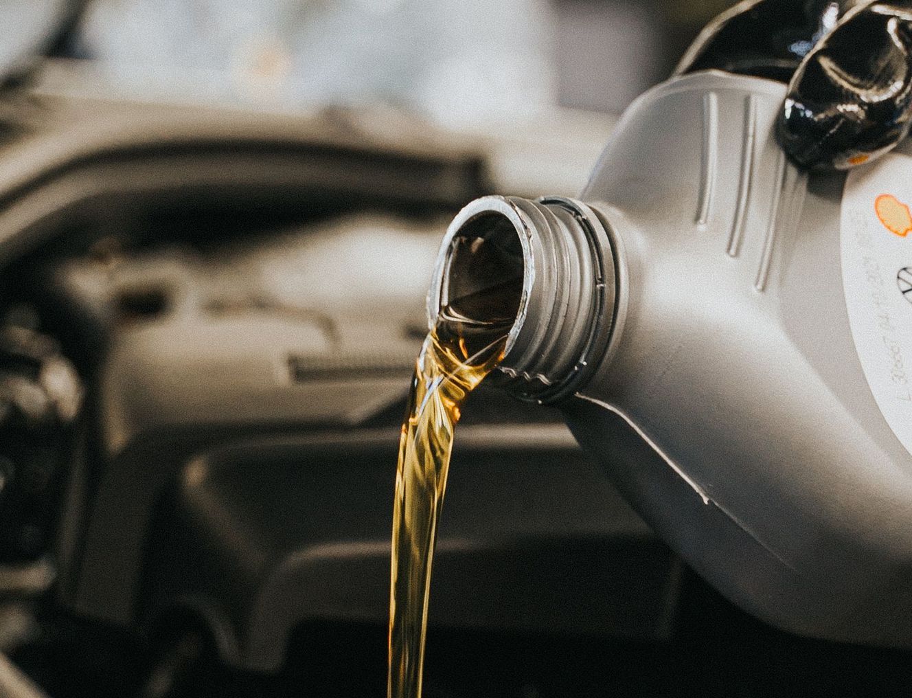 Close-up of a mechanic's gloved hand pouring engine oil into a vehicle.