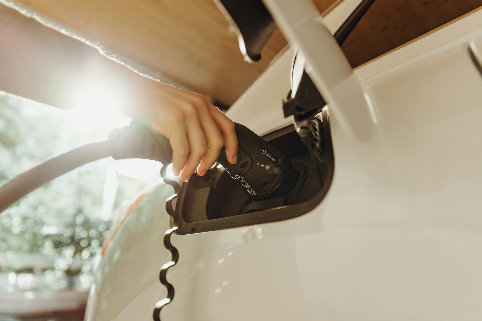 A hand plugging a charging cable into a white electric vehicle